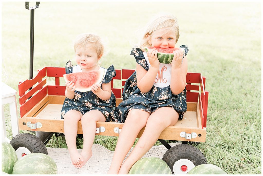 two little girls sitting in wagon eating watermelon