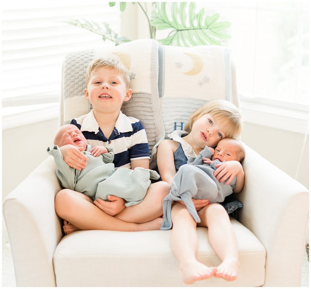 older sister and brother sitting together holding newborn siblings