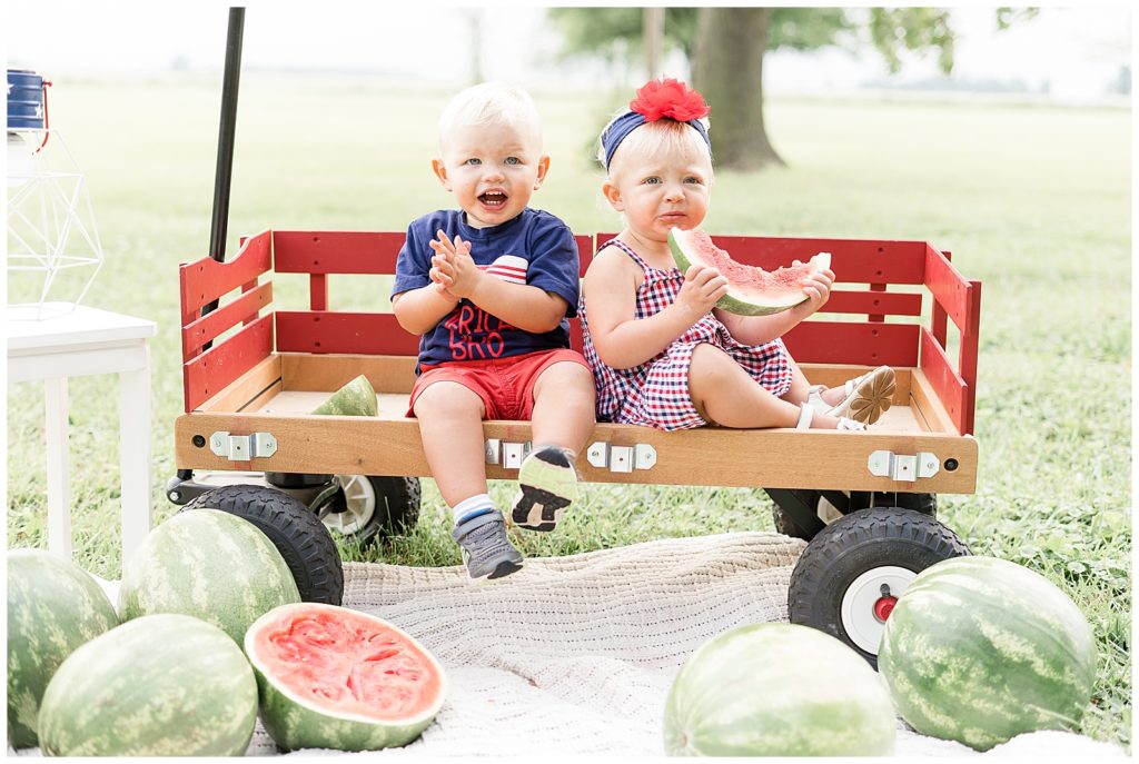little boy and girl sitting in wagon clapping and eating watermelon